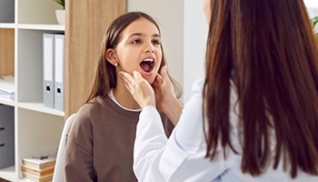 Eine Ärztin untersucht den Rachen einer Patientin und tastet die Mandeln ab